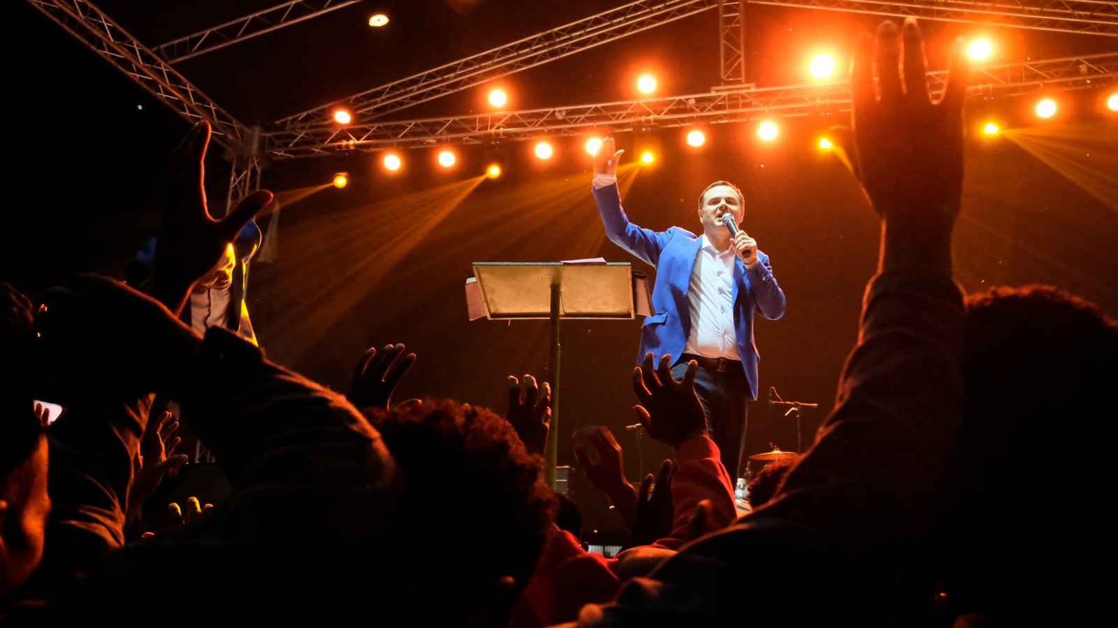 A ministry leader addressing a large worship gathering from a stage.