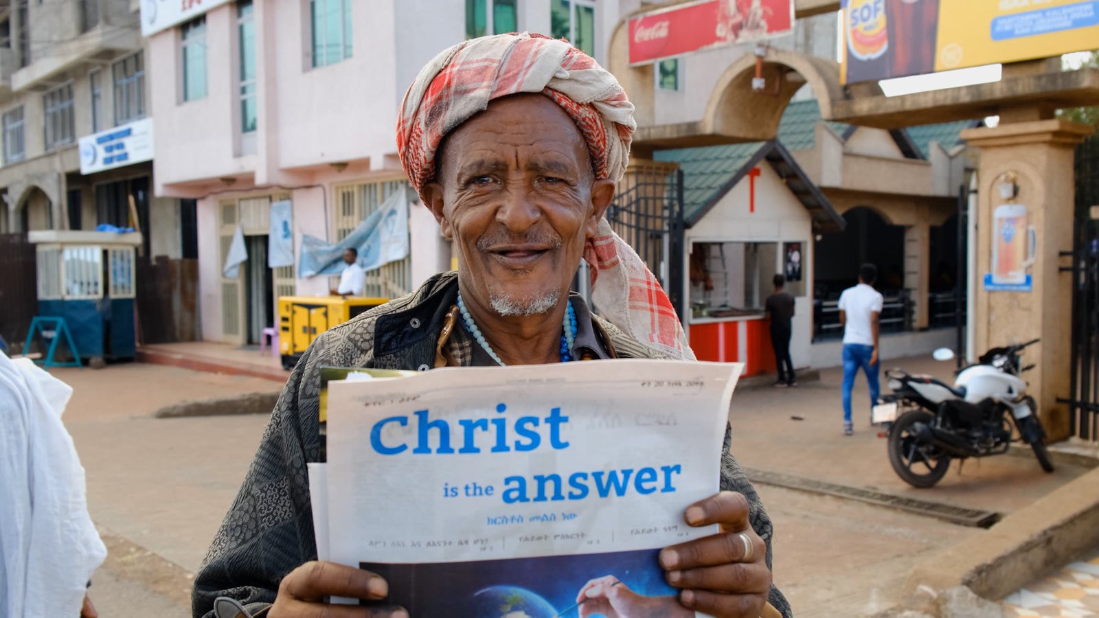 A man holding a Christ Is the Answer newspaper in a city street.